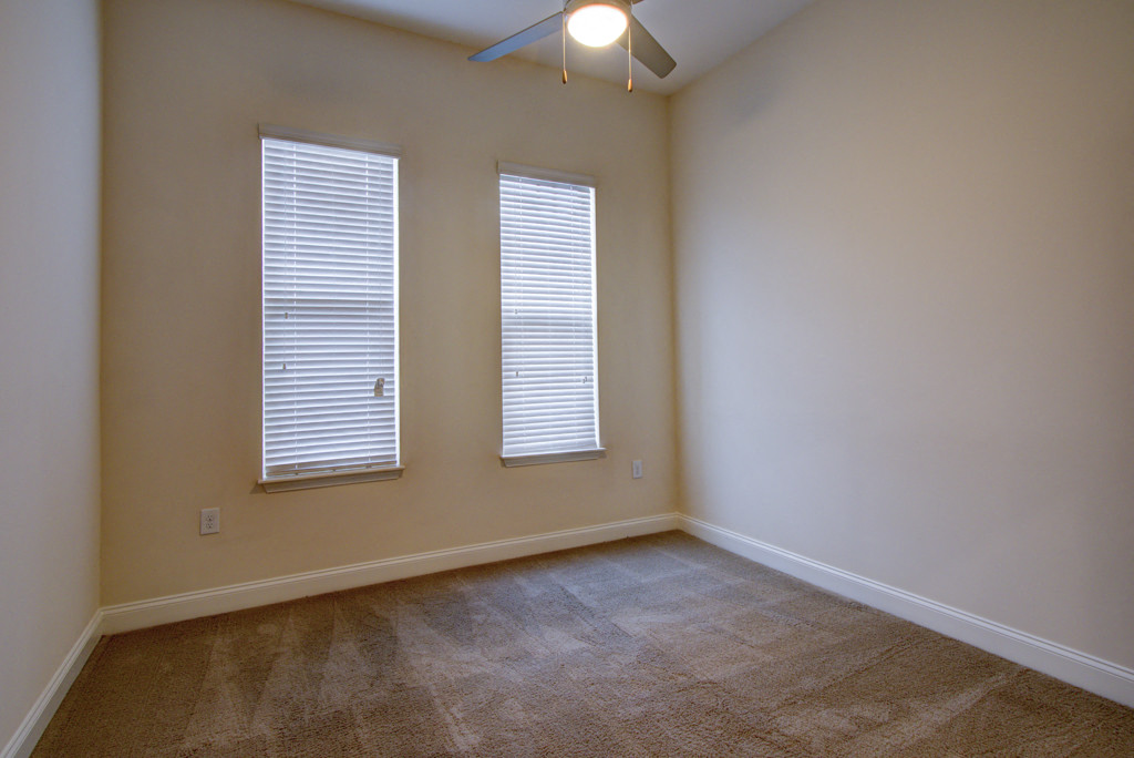 an empty living room with two windows and a ceiling fan