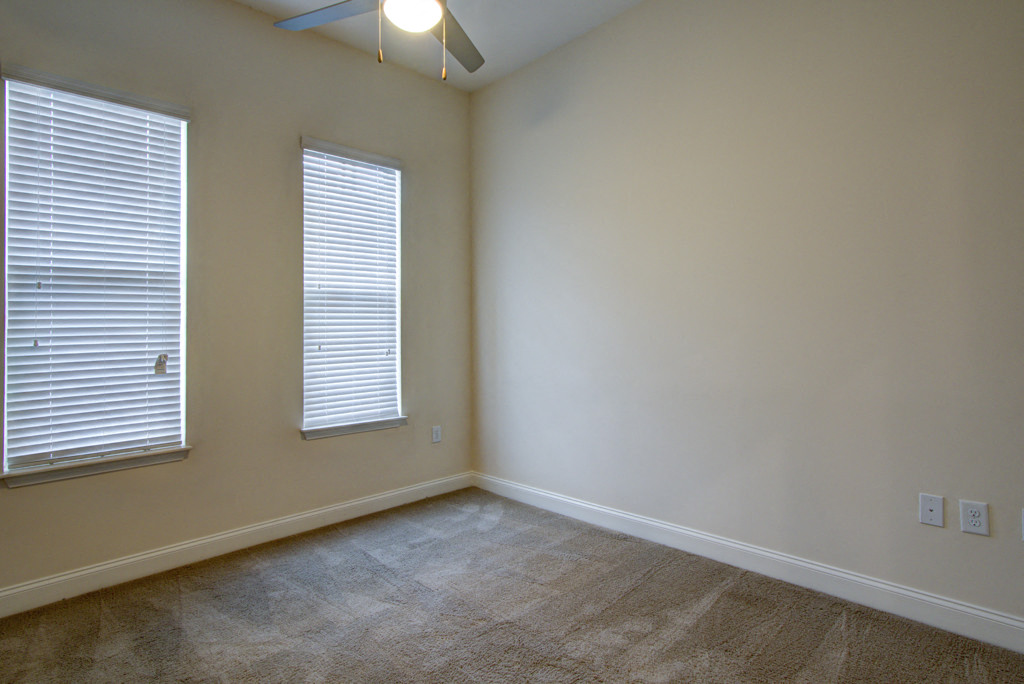 an empty living room with two windows and a ceiling fan