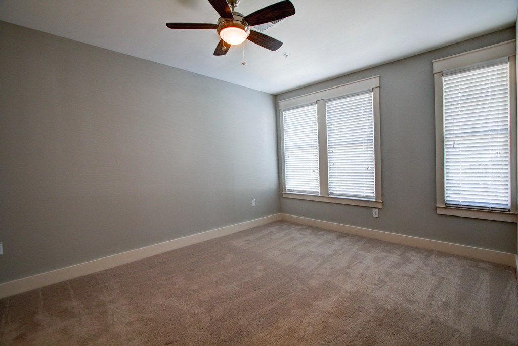 an empty room with a ceiling fan and two windows