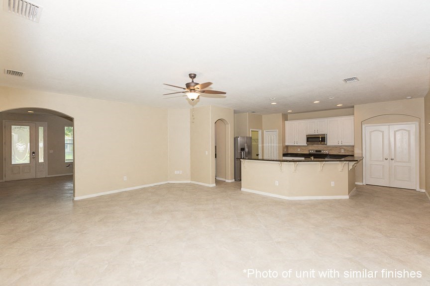 A spacious living room with a ceiling fan and a kitchen area in the background.