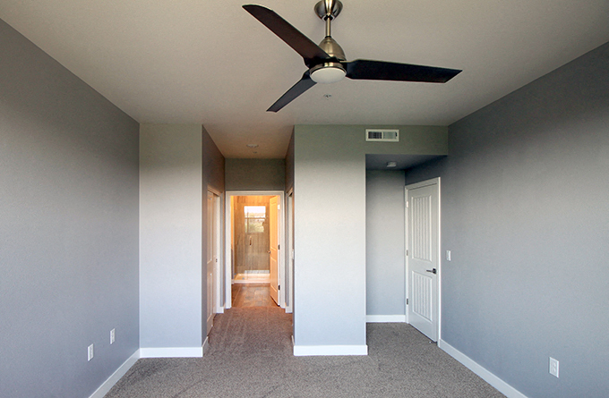 Reno Apartments - Park Place - Bedroom with Plush Carpeting, a Ceiling Fan and a Hallway Leading Toward the Bathroom