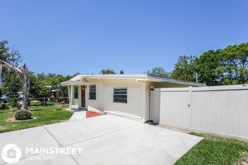 a small white house with a driveway and a white fence