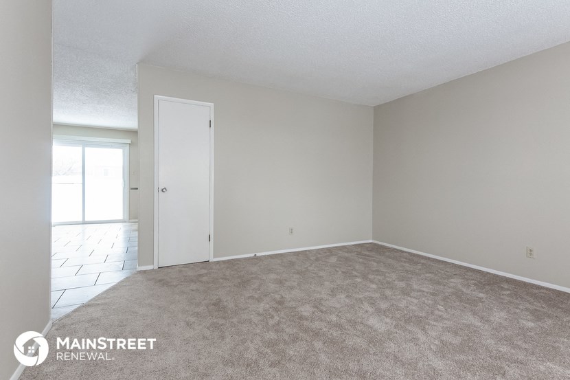 an empty living room with a rug and a door to the kitchen