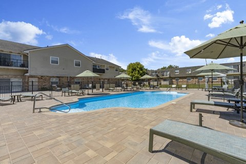 a swimming pool with tables and umbrellas at an apartment complex