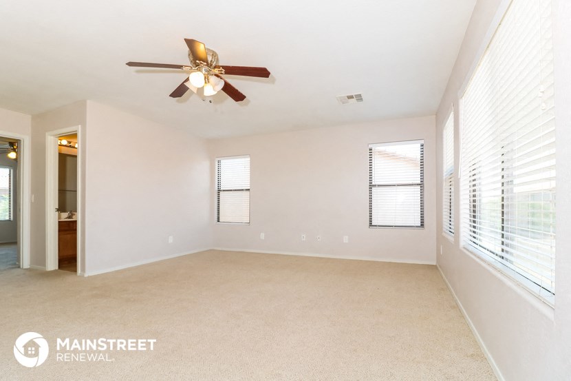 an empty living room with a ceiling fan and large windows