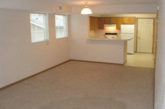 an empty living room and a kitchen with a refrigerator