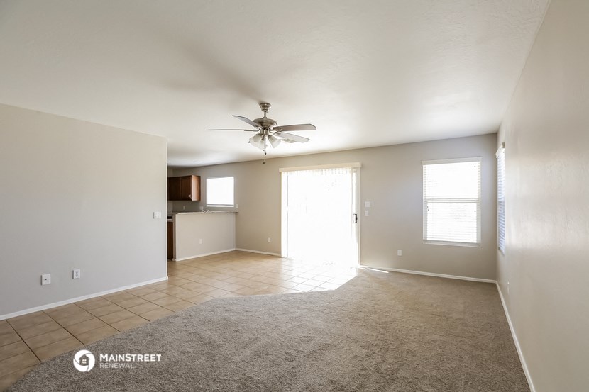 an empty living room with a ceiling fan and a kitchen