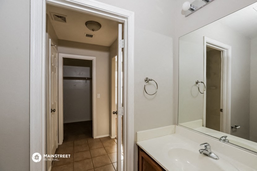 a bathroom with a sink and a mirror and a hallway to a closet