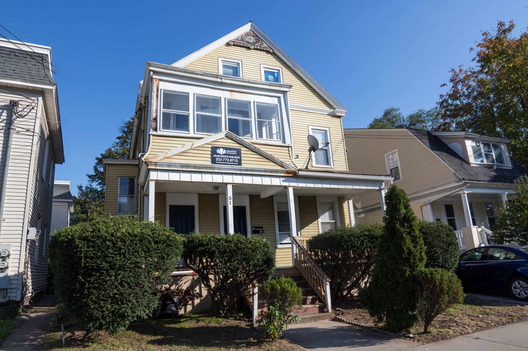 A two-story house with a front porch and a car parked in the driveway.