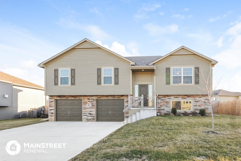 a beige and brick house with a driveway and grass