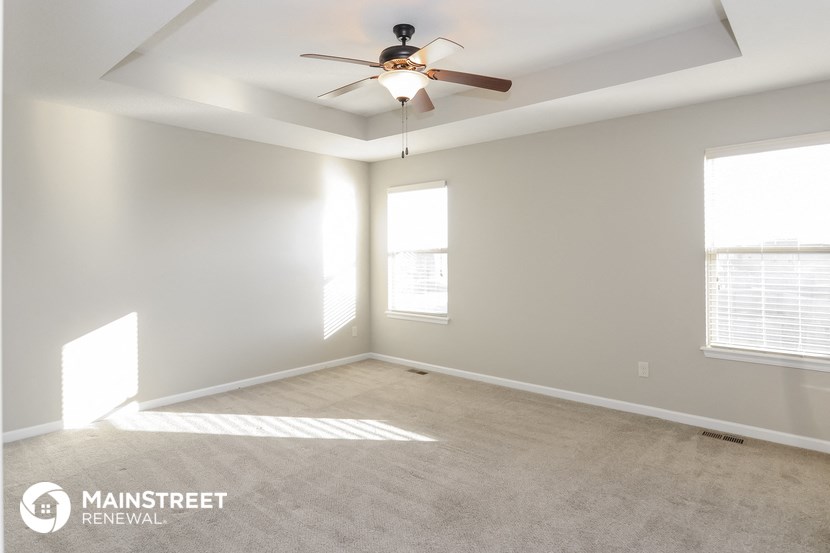an empty room with a ceiling fan and two windows