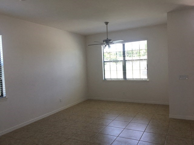 an empty living room with a ceiling fan and a tiled floor