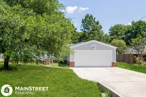 a small white garage with a driveway and a tree