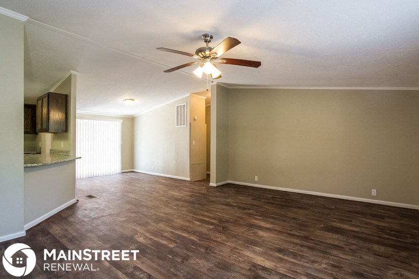 an empty living room with a ceiling fan and a kitchen