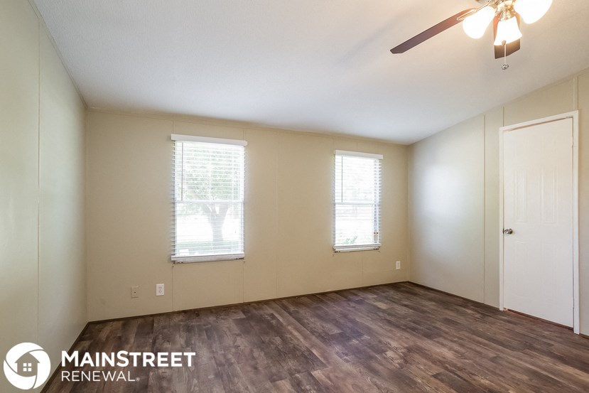 the spacious living room with wood flooring and a ceiling fan