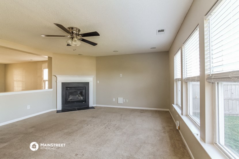 an empty living room with a fireplace and a ceiling fan