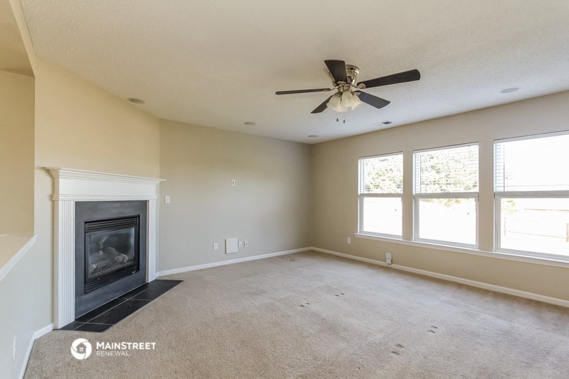 an empty living room with a fireplace and a ceiling fan