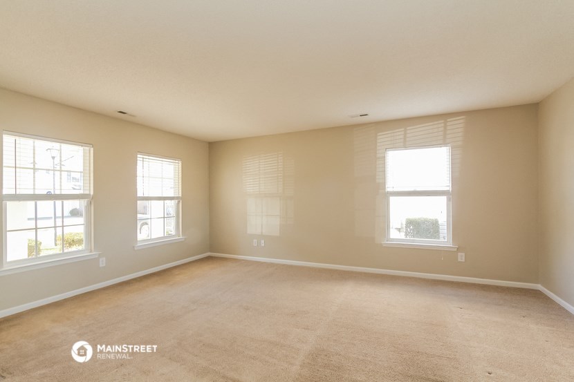 the spacious living room of a home with three windows