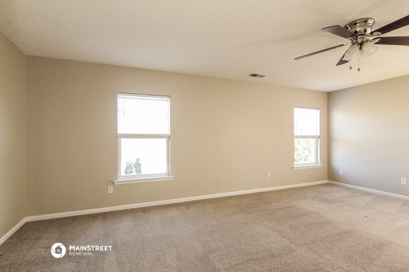 an empty living room with a ceiling fan and two windows