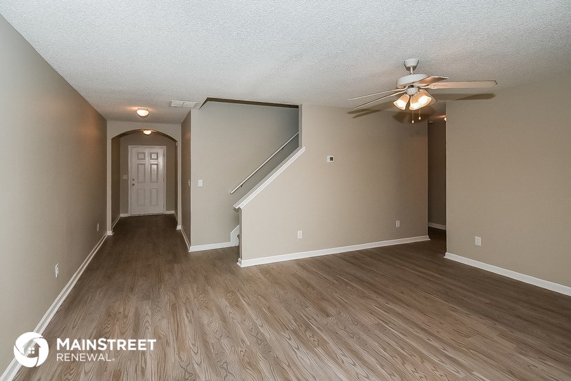 the living room and dining room of an apartment with wood floors and a ceiling fan