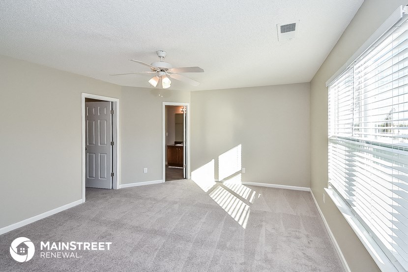 a spacious living room with large windows and a ceiling fan