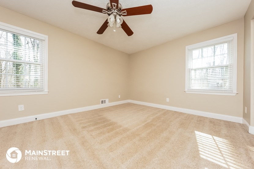 an empty living room with a ceiling fan and two windows