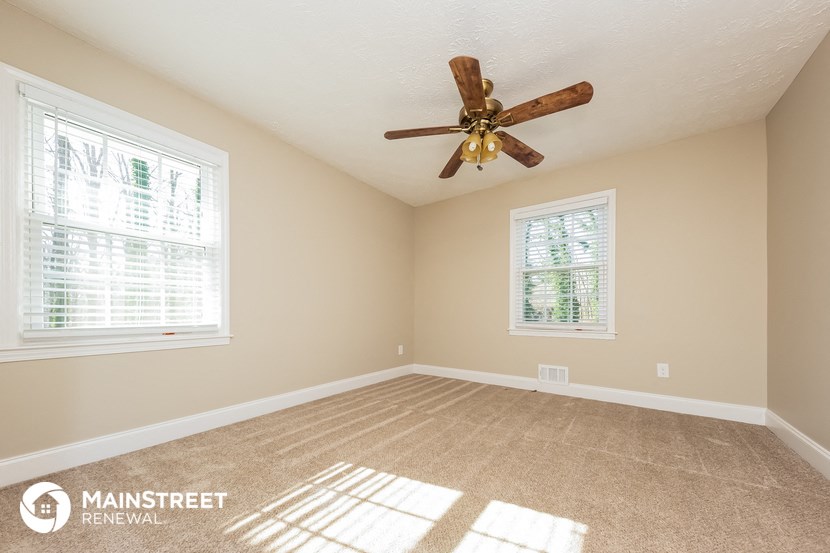an empty living room with a ceiling fan and two windows