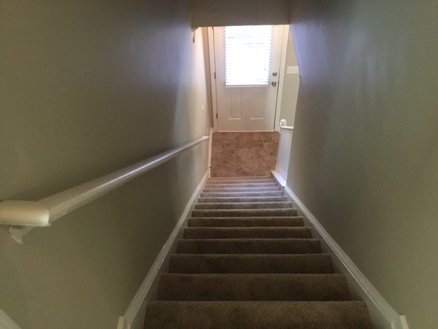 the stairway up to a white door and stairs leading to a hallway with carpet