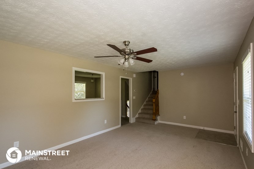 an empty living room with a ceiling fan and a staircase