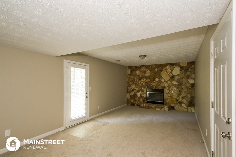 an empty living room with a stone fireplace and a door to the dining room