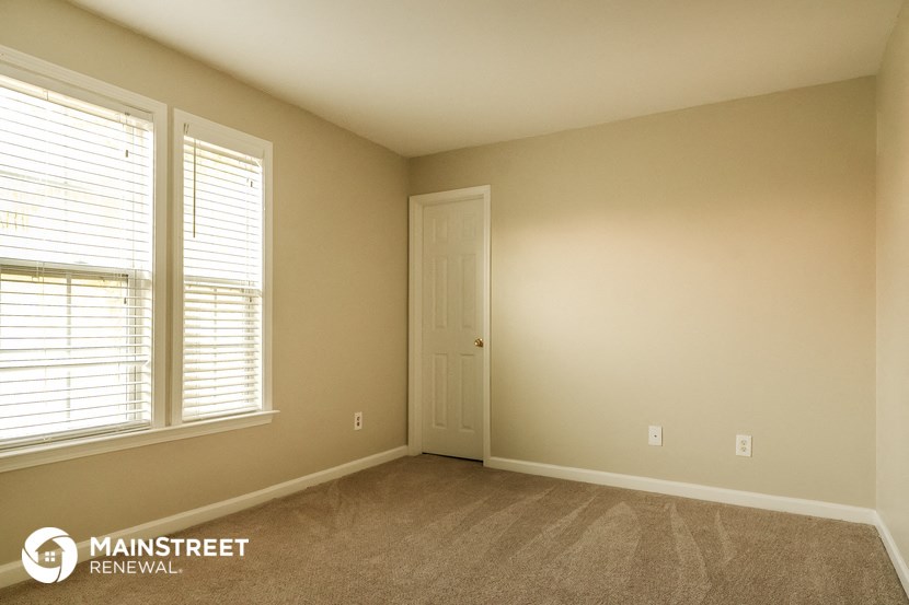 a bedroom with a door and two windows and a carpeted floor