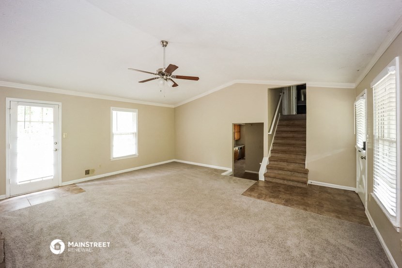 an empty living room with a ceiling fan and a staircase