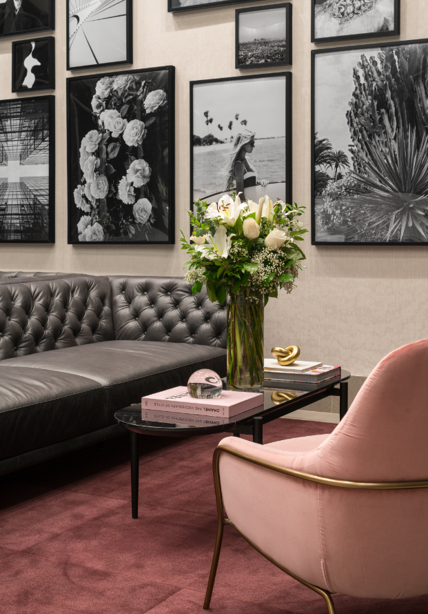 A living room with a grey sofa, a pink chair, a coffee table with a book and a vase with flowers.