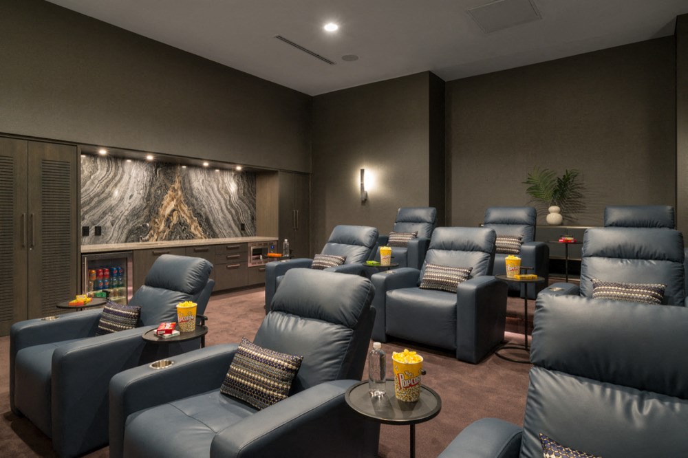 A row of blue recliner chairs are arranged in a room with a wall mural and a table with a yellow cup on it.