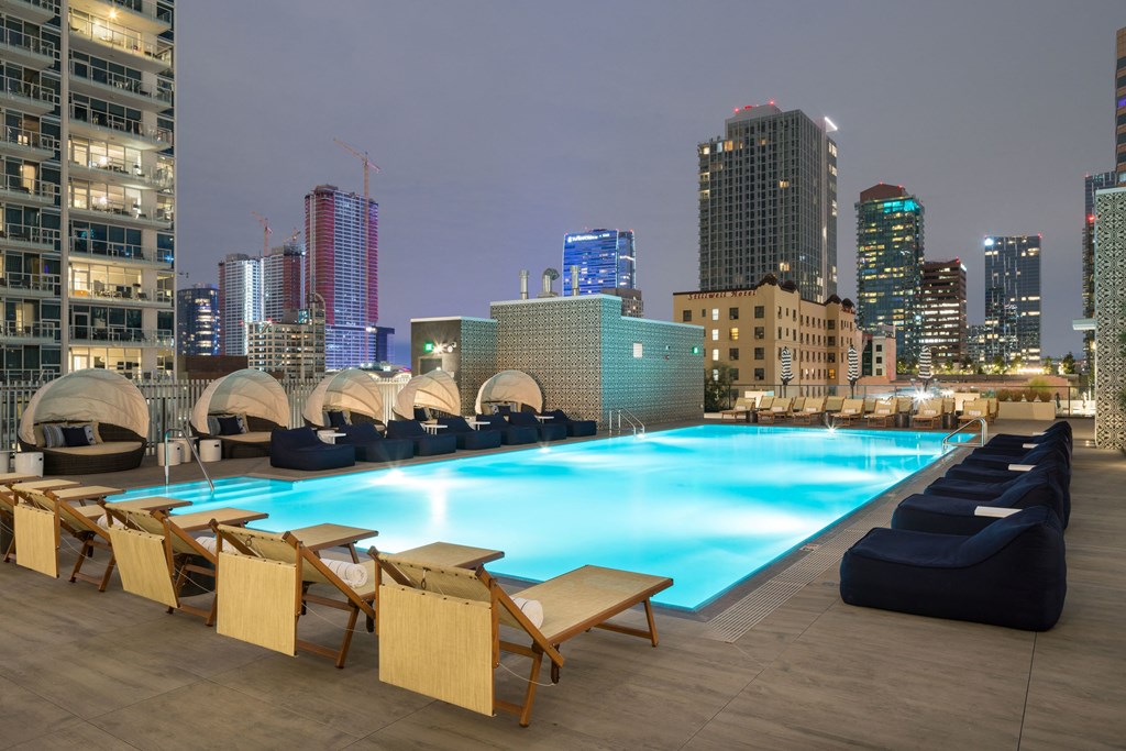 A pool with chairs and umbrellas on a terrace with a city skyline at night.