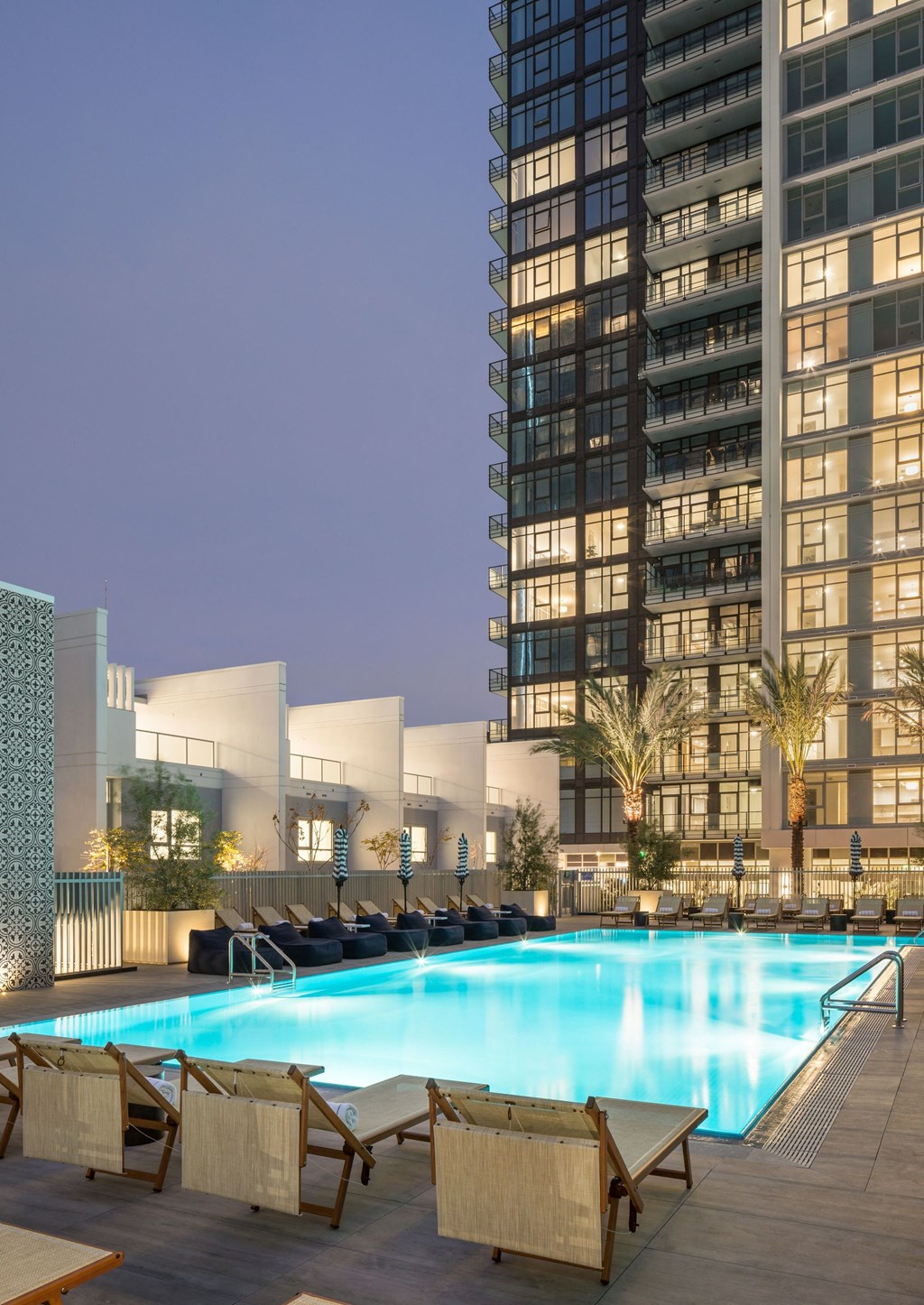 A swimming pool surrounded by chairs and a tall building in the background.