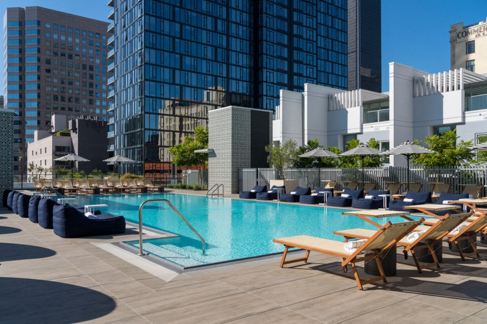 A pool surrounded by lounge chairs and umbrellas with buildings in the background.