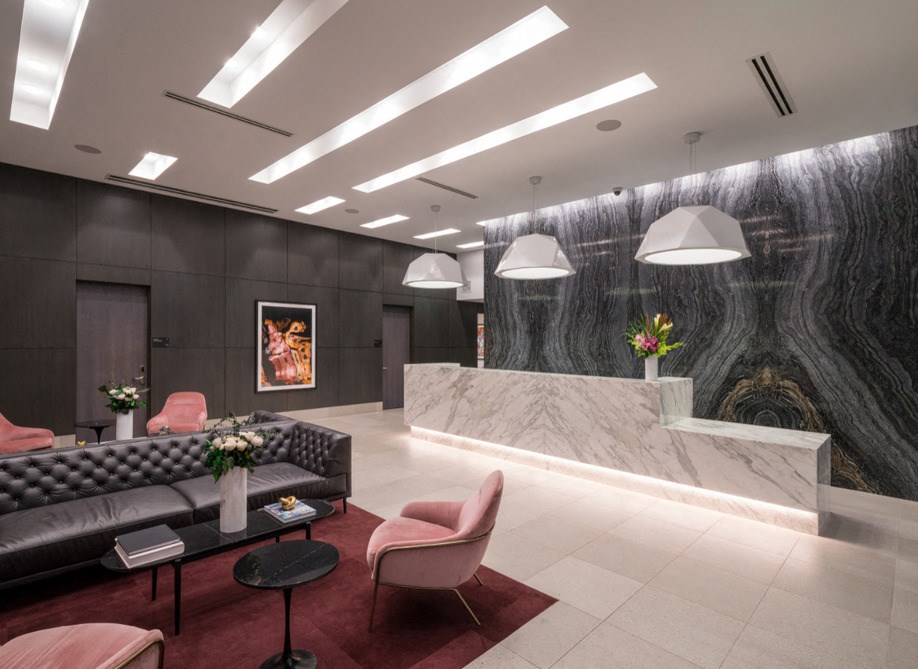 A modern living room with a black couch, pink chairs, and a marble wall.