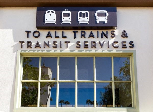 A sign that reads "To all trains & transit services" is above a window.