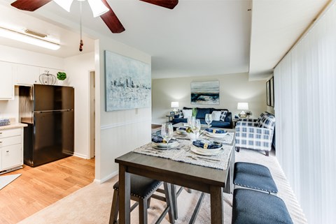 A dining area with a table set for two and a refrigerator in the corner.