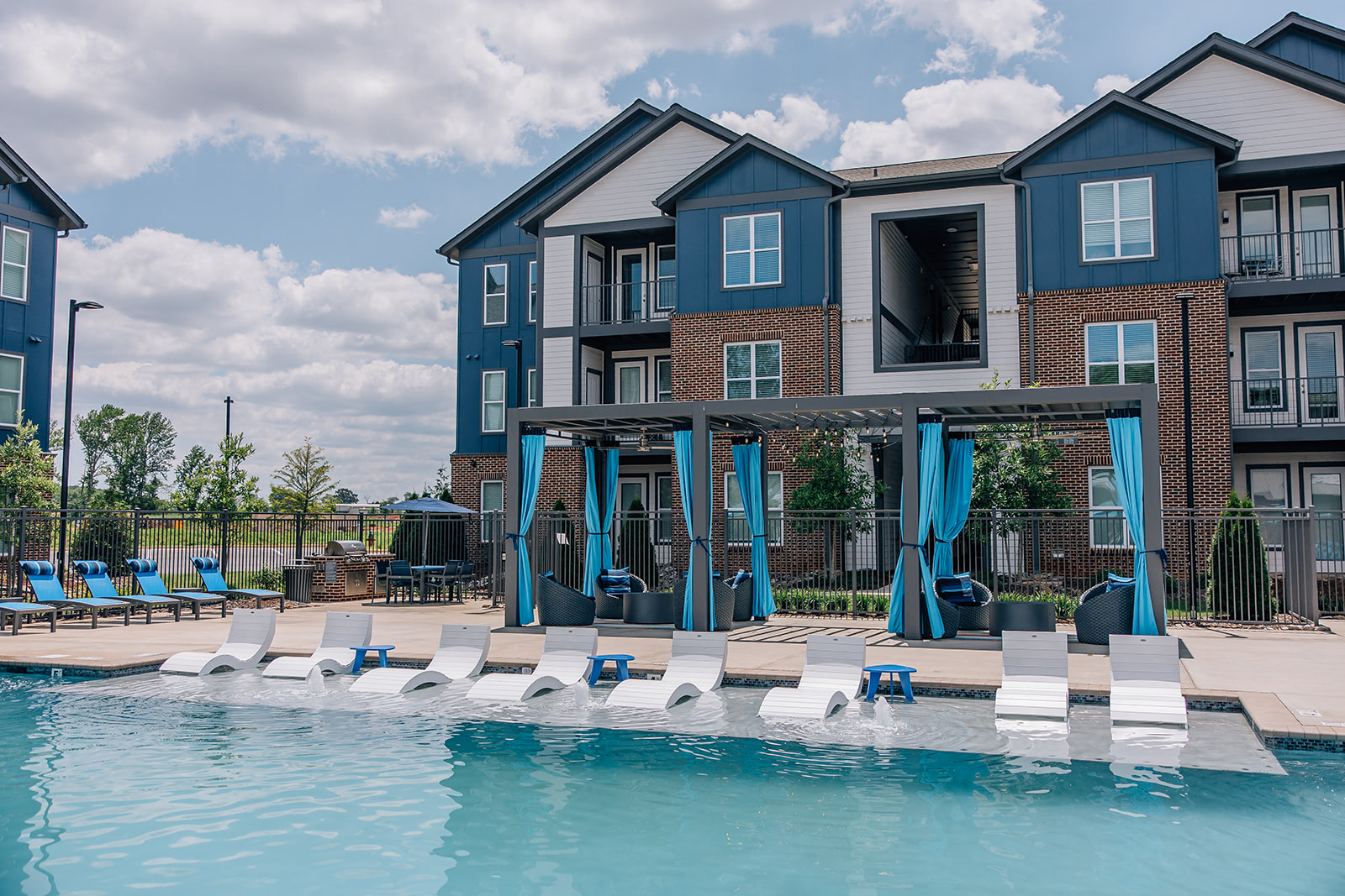 A swimming pool in front of a multi-story building with blue umbrellas.