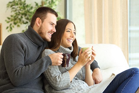 a man and woman sitting on a couch holding coffee cups