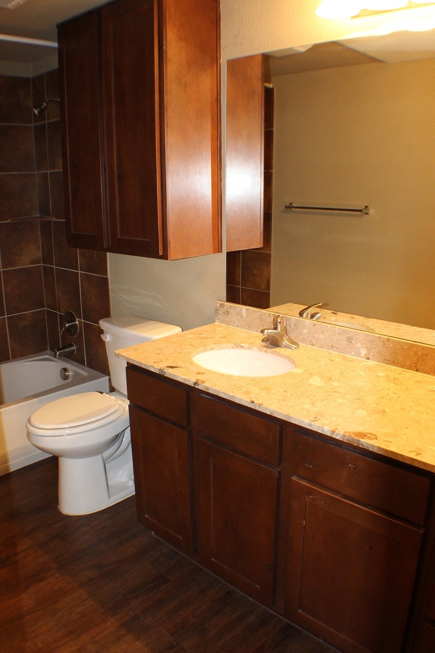 A bathroom with a toilet, sink, and brown cabinets at City Place Apartments TX, 76201