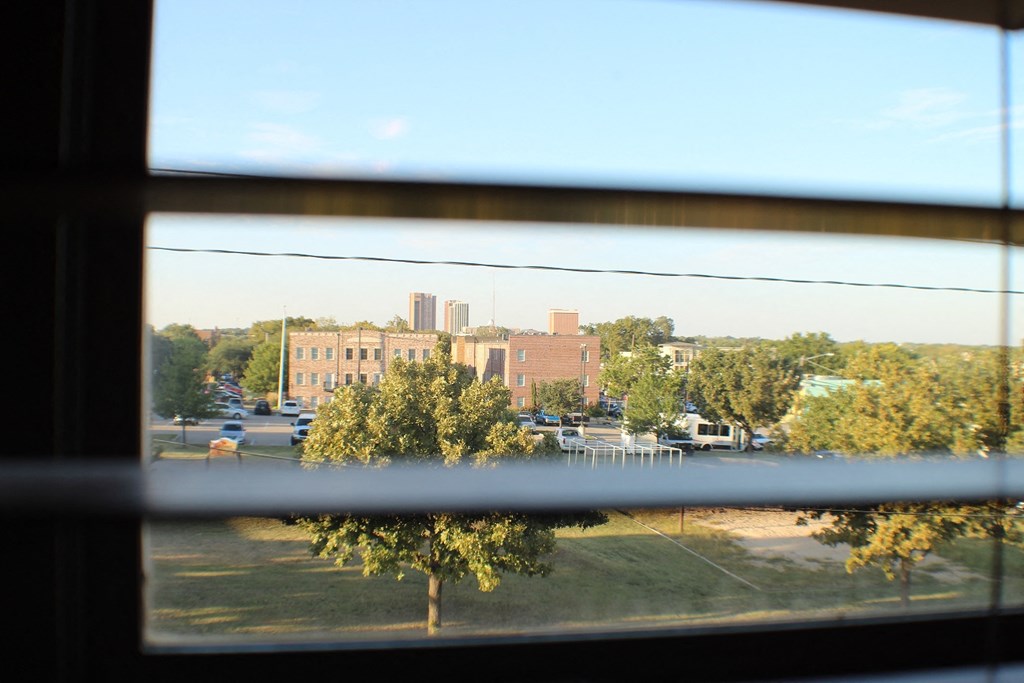 A view of a building through a window with trees in the foreground at City Place Apartments, Denton, 76201
