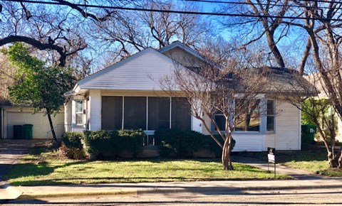 A house with a white siding and a grey roof is surrounded by trees.