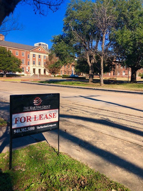 A Marting Group for lease sign is in the foreground of a parking lot.