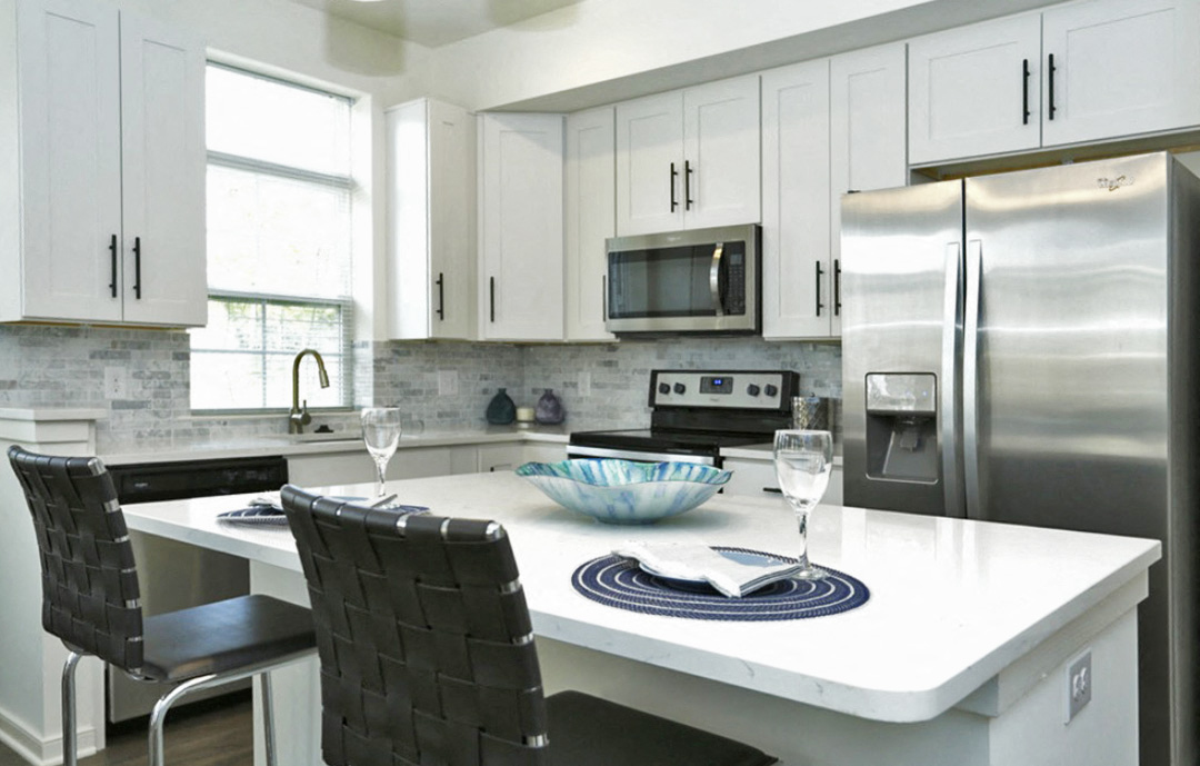 a white kitchen with stainless steel appliances and a white island with black chairs