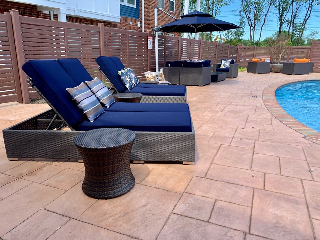 a poolside patio with blue lounge chairs and umbrellas next to a pool