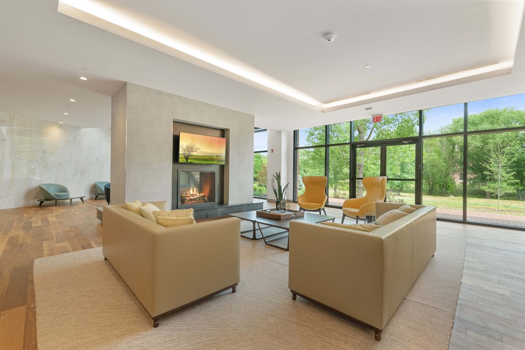 A community lounge with  a fireplace, comfortable chairs and panoramic windows with beautiful views of green space. at Keva Flats, Exton, PA, 19341