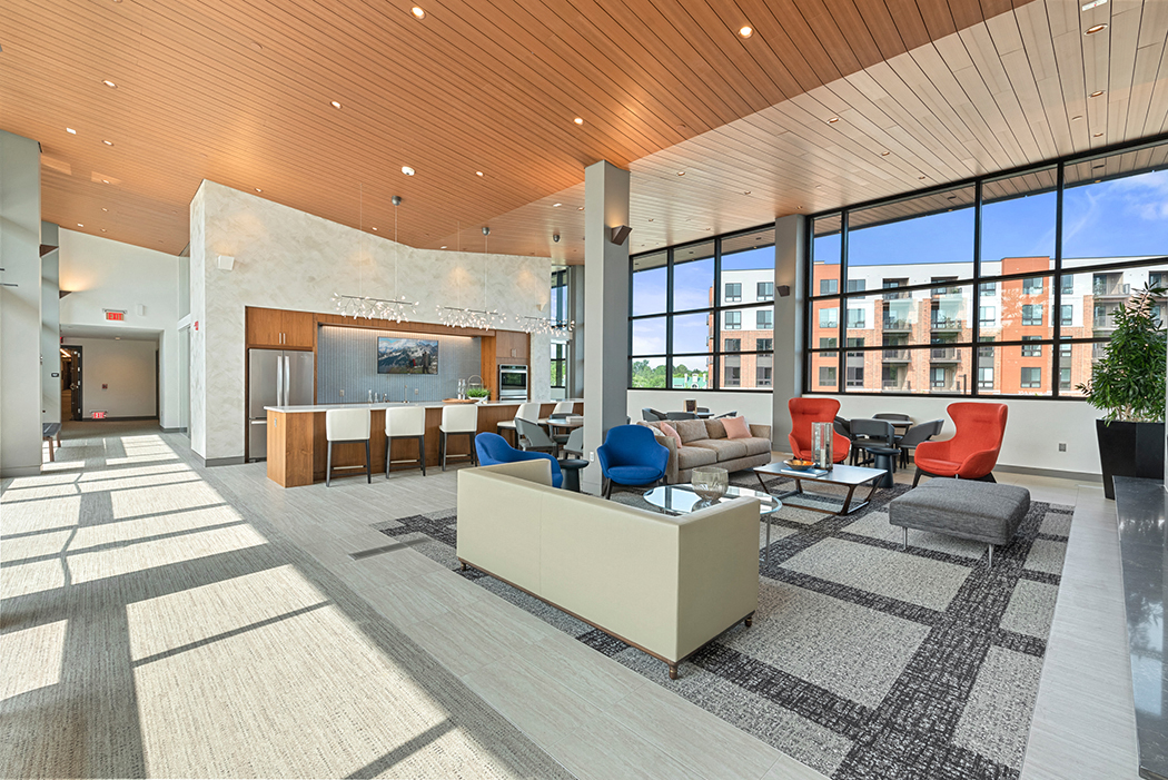 The lower level of a 2-story clubhouse with high ceilings, large panoramic windows, a community kitchen, and a comfortable lounge area. at Keva Flats, Pennsylvania